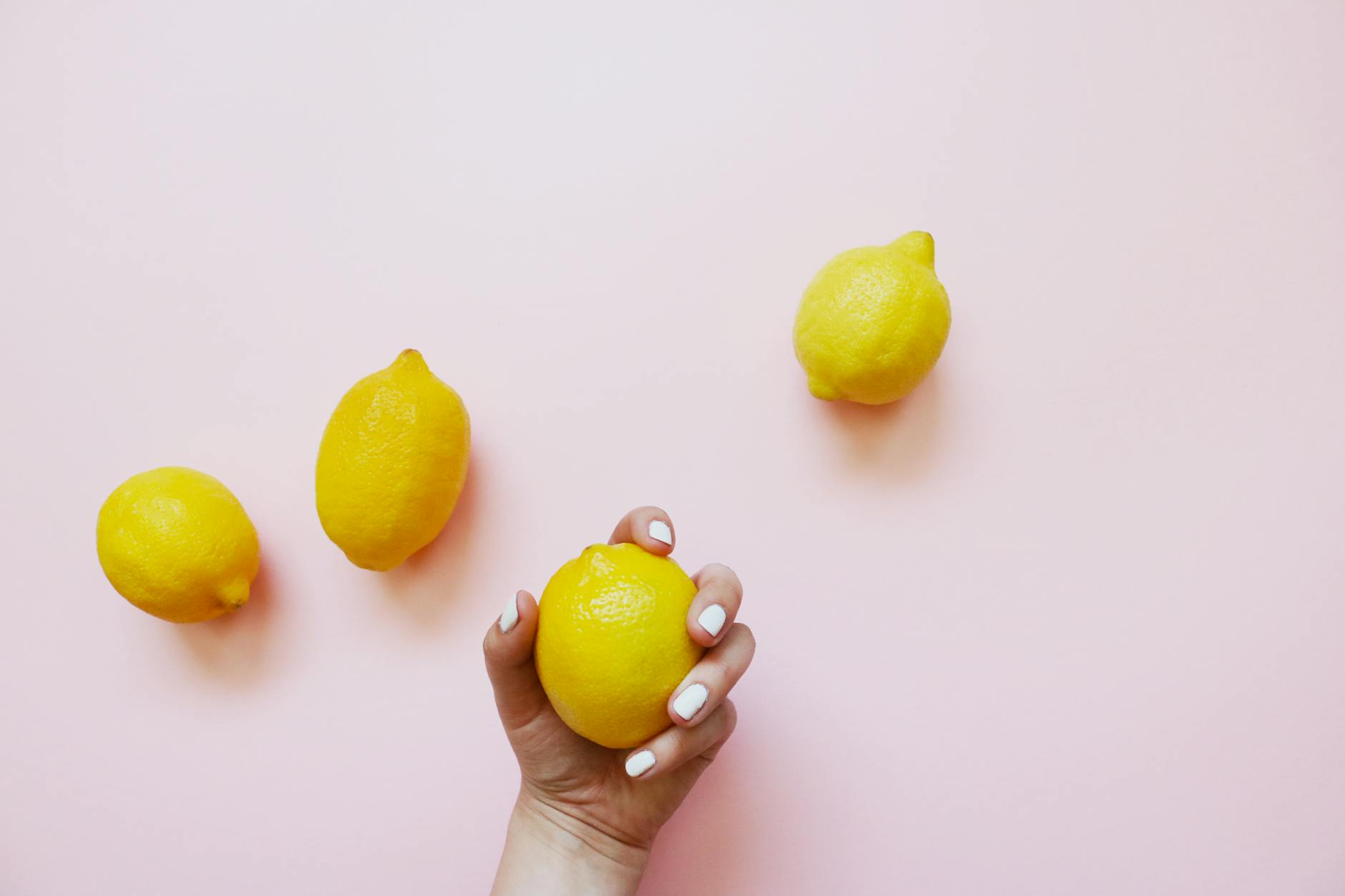 Hand holding a bright lemon on a soft pink background, symbolizing gentle, delicate sensation