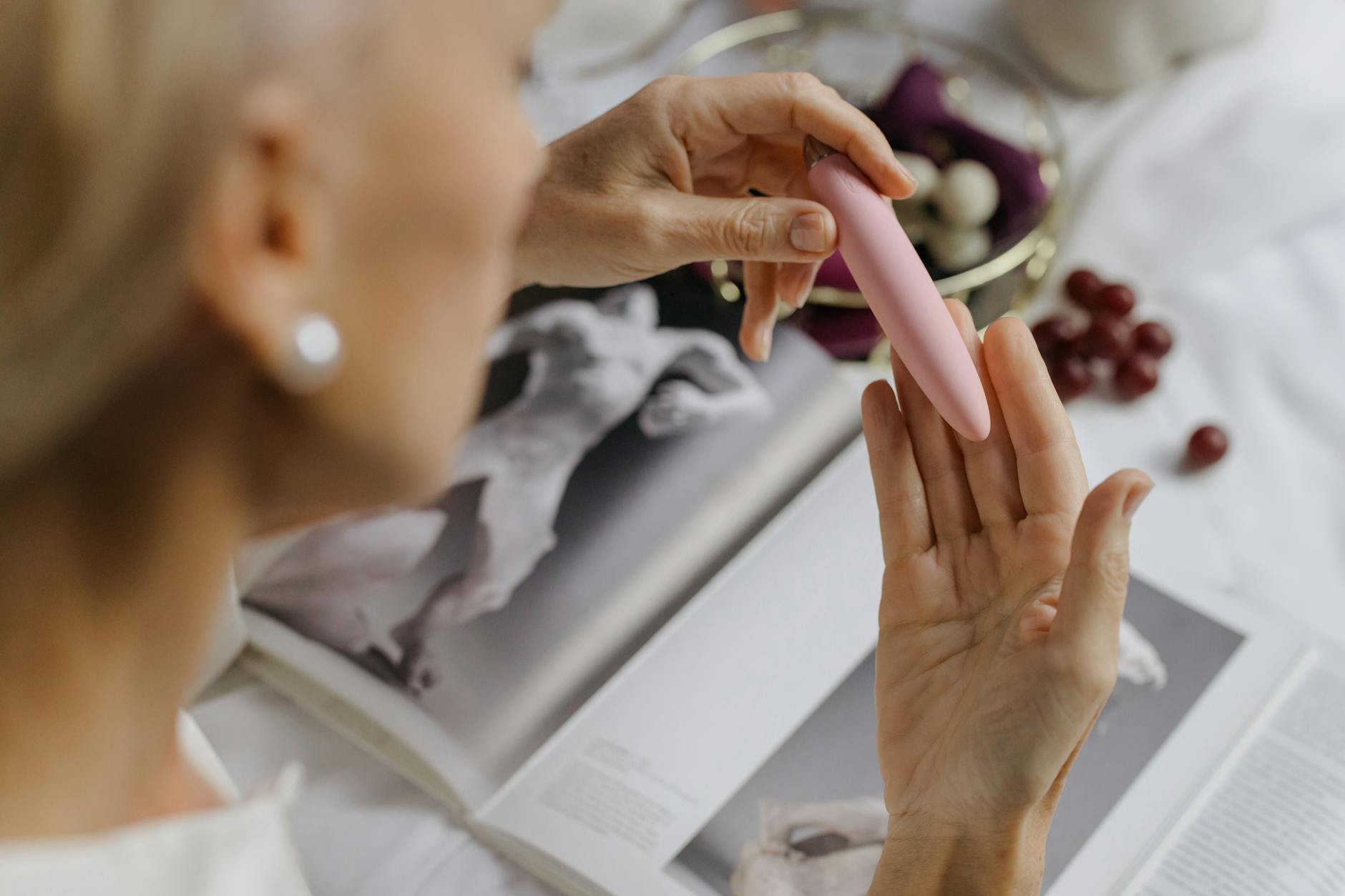 Close-up of a woman holding a pink vibrator in a quiet, intimate moment with art books nearby
