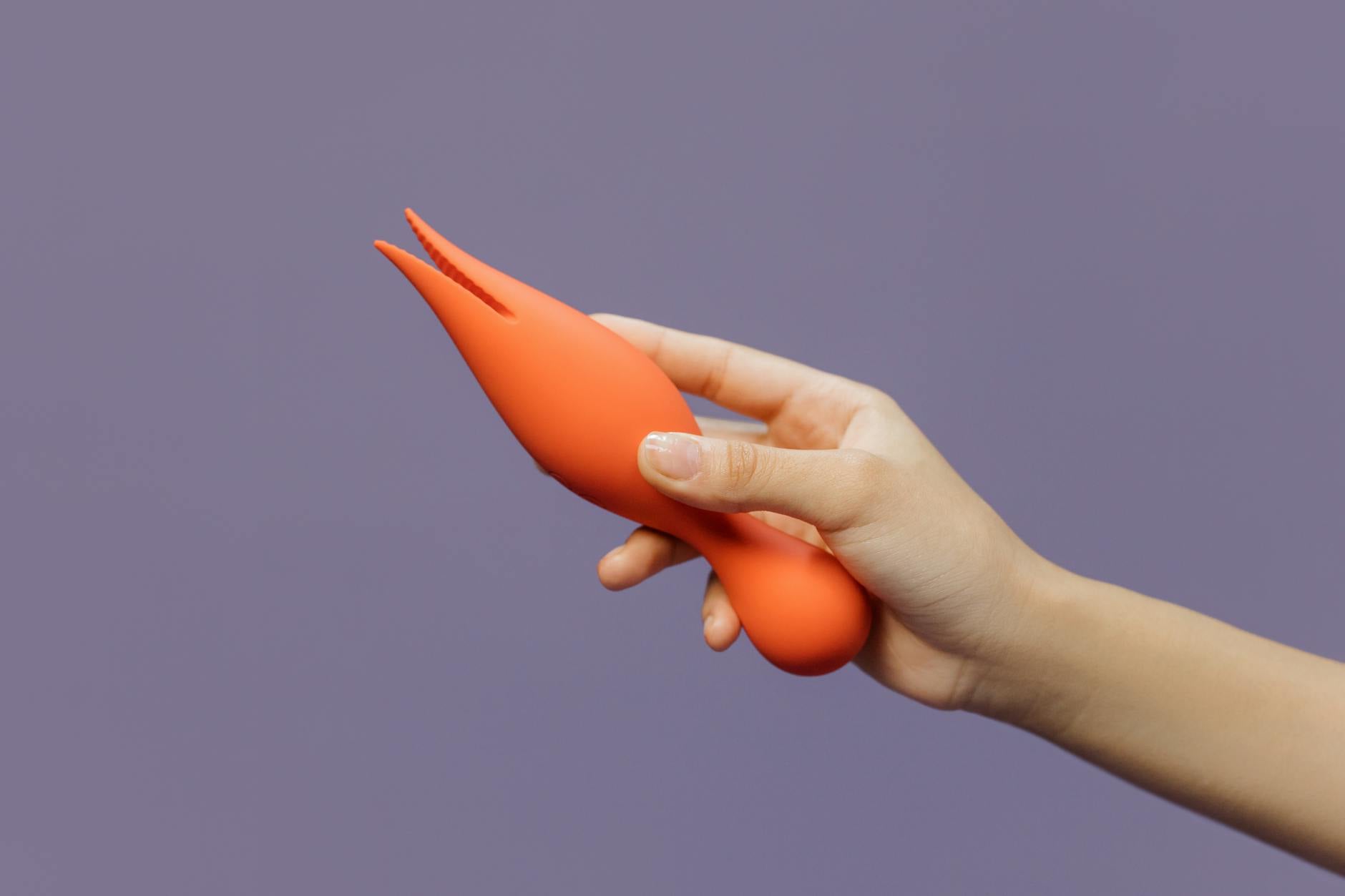 A hand holding a yellow lemon vibrator against a purple minimalist backdrop