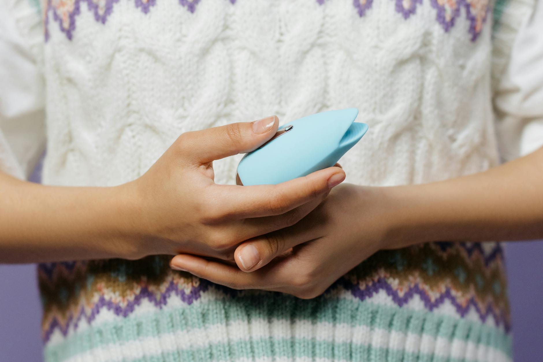 Hands holding a blue personal massager against a knitted sweater, representing gentle reintroduction to pleasure.